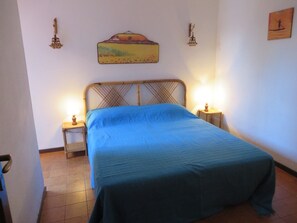 Ein Einzelbett mit blauer Bettdecke, zwei Nachttischlampen, ein Wandbild und ein kleiner Tisch mit Lampe.