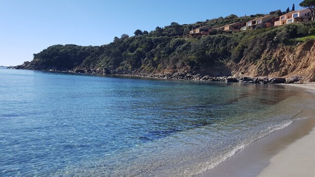 A coastal beach with clear water, a sandy shore, and hillside buildings. - Sea View House Near the Beach – Casa Accu is Prezzus F (Villasimius)