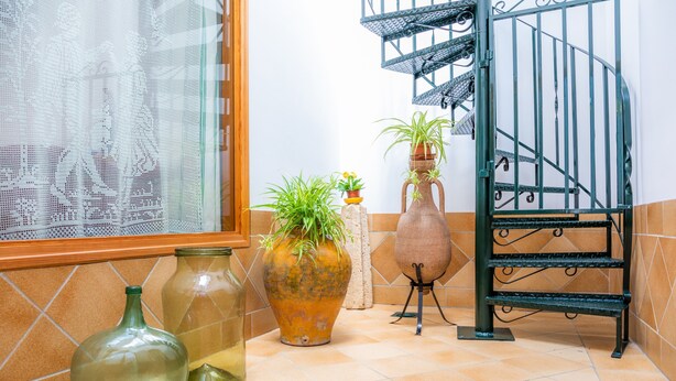 Une cuisine avec un carrelage au sol, une fenêtre ornée de rideaux en dentelle et un escalier avec une rampe en métal.