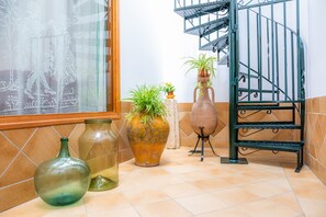 A kitchen with tiled flooring, a window with lace curtains, and a staircase with a metal railing. - Holiday home with exclusive interior, pool and garden perfect for cyclists (Sa Pobla)