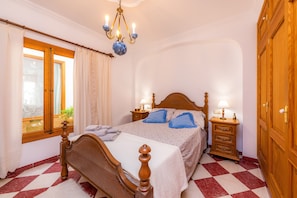 A bedroom with a wooden bed, two bedside tables with lamps, a window with curtains, and a wooden wardrobe.