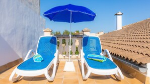 Deux chaises longues avec des coussins bleus, un parasol bleu et un toit recouvert de tuiles.
