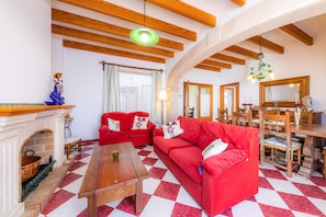 A living room with a checkered floor, red sofas, a wooden table, a fireplace, and a dining area with wooden furniture.