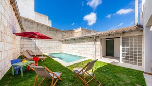 Un jardin avec une piscine, des chaises longues et une table avec un parasol.