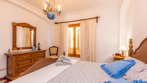 Une chambre à coucher comprenant un lit, une commode, un miroir, une table de chevet et une fenêtre avec des rideaux.