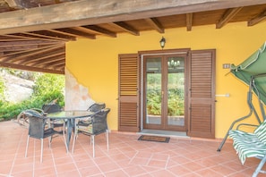 A covered patio with a table and chairs, a door with shutters, and a green umbrella.