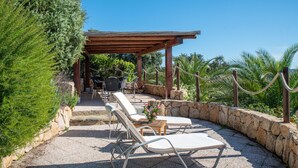 A covered outdoor seating area with lounge chairs, a table with flowers, and a stone wall.