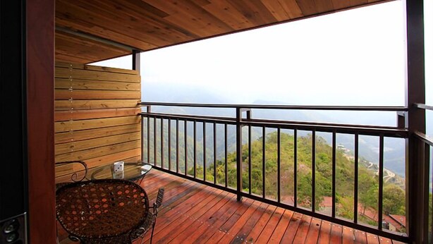 A wooden balcony with a metal railing, a wicker chair, and a view of a mountainous landscape. - Stream Yurt Campground (Ren'ai)