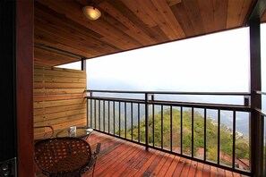 A wooden balcony with a metal railing, a wicker chair, and a view of a mountainous landscape. - Stream Yurt Campground (Ren'ai)