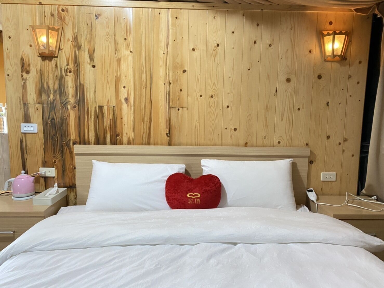 A wooden-paneled room with a bed, two bedside tables, and two wall-mounted lamps.