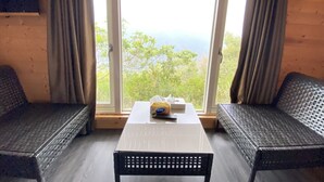 A room with a large window, two wicker chairs, a white table, and a black chair. - Stream Yurt Campground (Ren'ai)