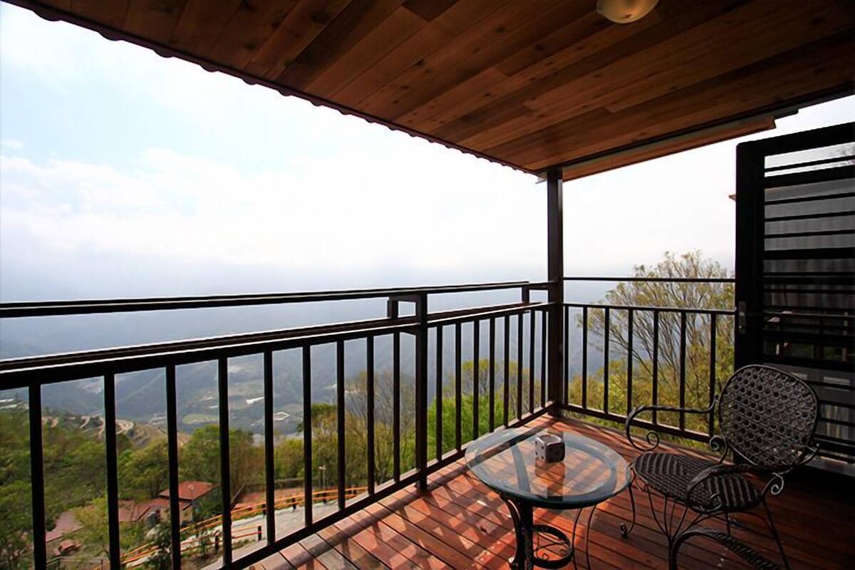 Una terraza de madera con una mesa de vidrio y sillas de metal, con vistas a un paisaje pintoresco.