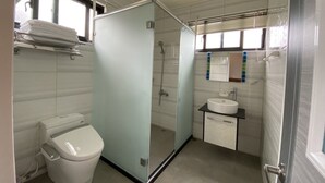 A modern bathroom with a toilet, a glass-enclosed shower, and a sink with a mirror. - Stream Yurt Campground (Ren'ai)