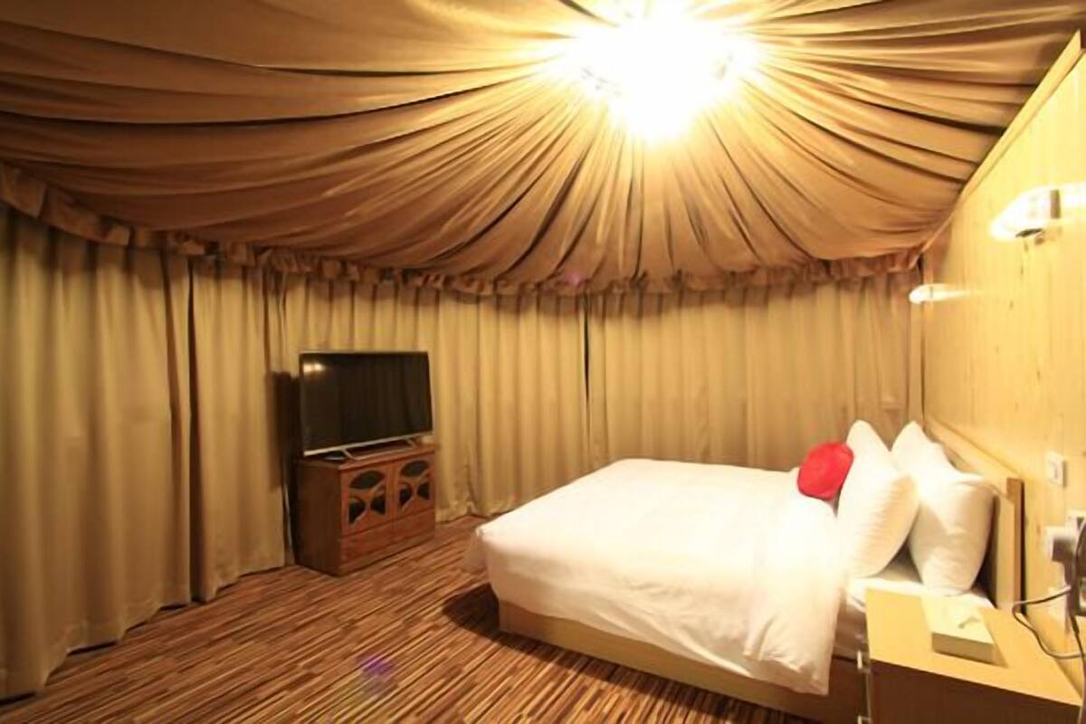 Una habitación de hotel con cama, cortinas, televisor y una mesita de noche de madera.
