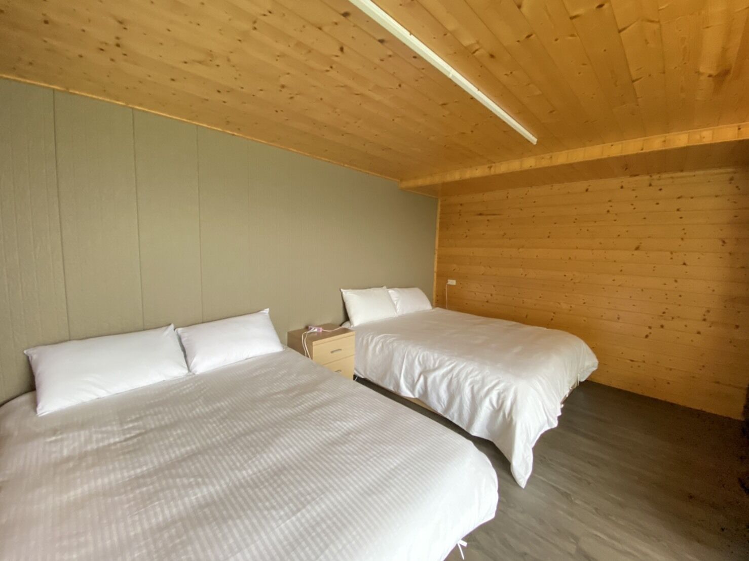 A room with two beds, wooden ceiling, and light-colored walls.