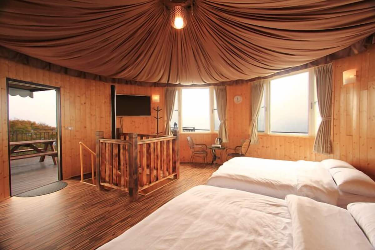 Habitación de cabaña de madera con dos camas, un escritorio de madera, una silla y un ventanal grande.