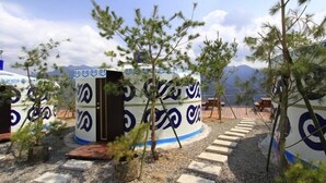 Yurts with blue and white patterns, arranged on a gravel path with trees in the foreground. - Stream Yurt Campground (Ren'ai)