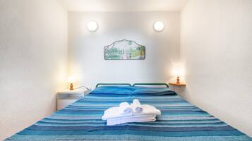 Ein Einzelbett mit blauen Streifen auf der Tagesdecke, zwei Nachttische mit Lampen und ein Wandbild.