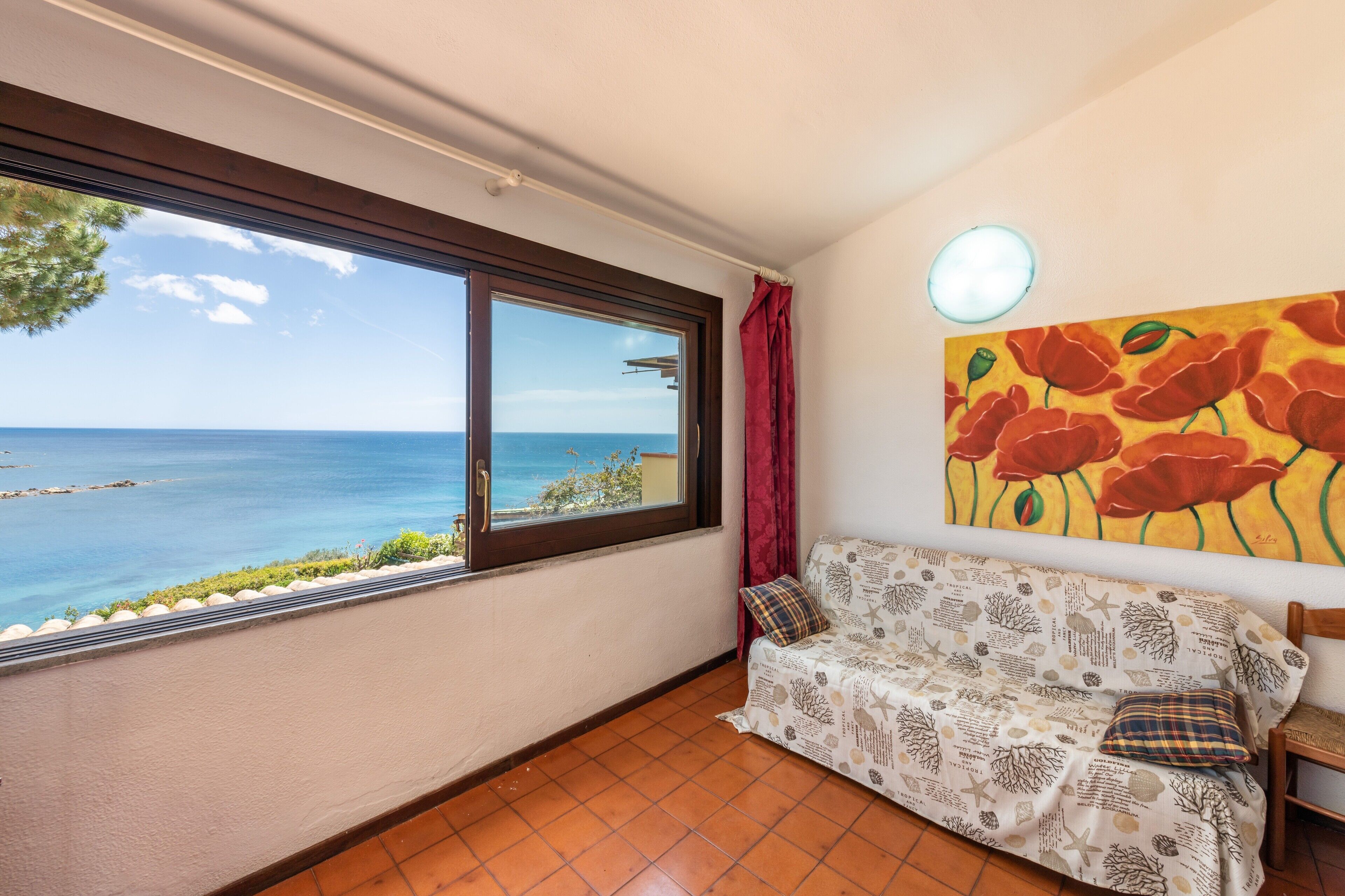 A room with a view of the sea, a sofa with a patterned cover, and a painting on the wall.