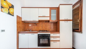 Eine kleine Küche mit weißen Schränken, einem eingebauten Backofen und einem Fenster mit Holzjalousien.