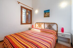 A bedroom with a bed, a nightstand, a bedside table, a window, and a wall-mounted picture. - Vacation home on the sea – Accu is Prezzus D (Villasimius Accu is Prezzus)