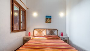 Ein Bett mit gestreifter Bettdecke, ein hölzernes Kopfteil, Nachttische mit roten Vasen und ein Bild an der Wand.