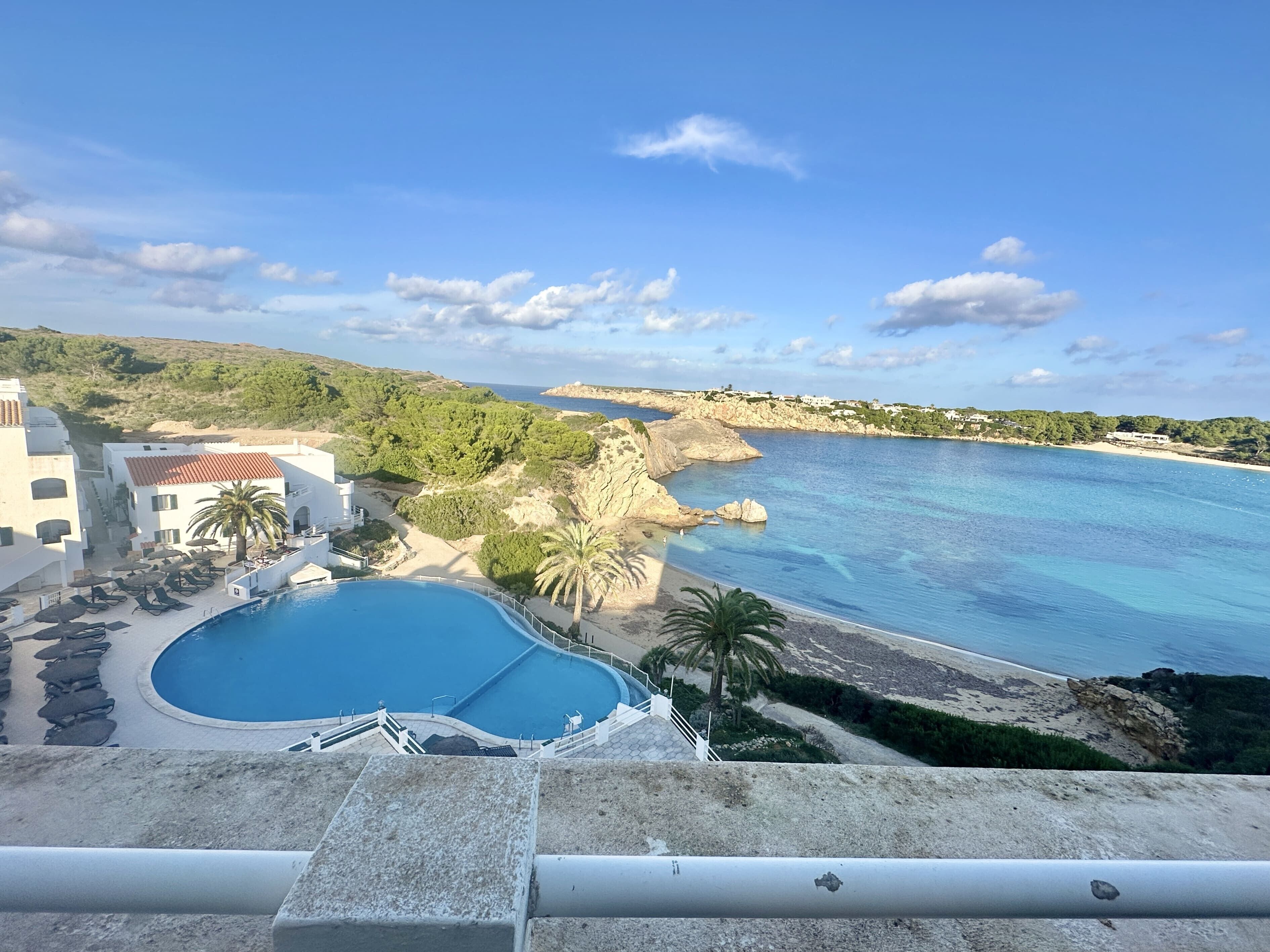 En pool med utsikt över havet, en byggnad med ett rött tak och en strand.