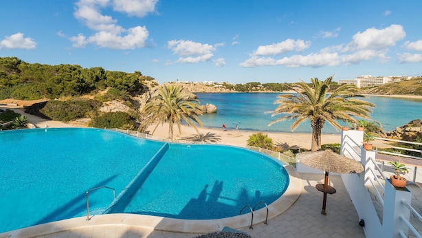 A swimming pool with a view of the sea, palm trees, and a beach. - Beautiful Apartment with Wi-Fi, Pool, Terrace and Sea View (Arenal d'en Castell)