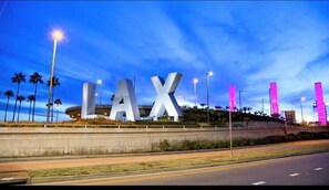 Un grand panneau « LAX » au design moderne, entouré de palmiers et de lampadaires.