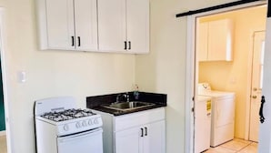 A compact kitchen with white cabinets, a gas stove, and a sink. - LAX guest house (Inglewood)