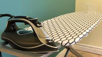 An ironing board with a patterned cloth, an iron, and a clear plastic cup on a table.