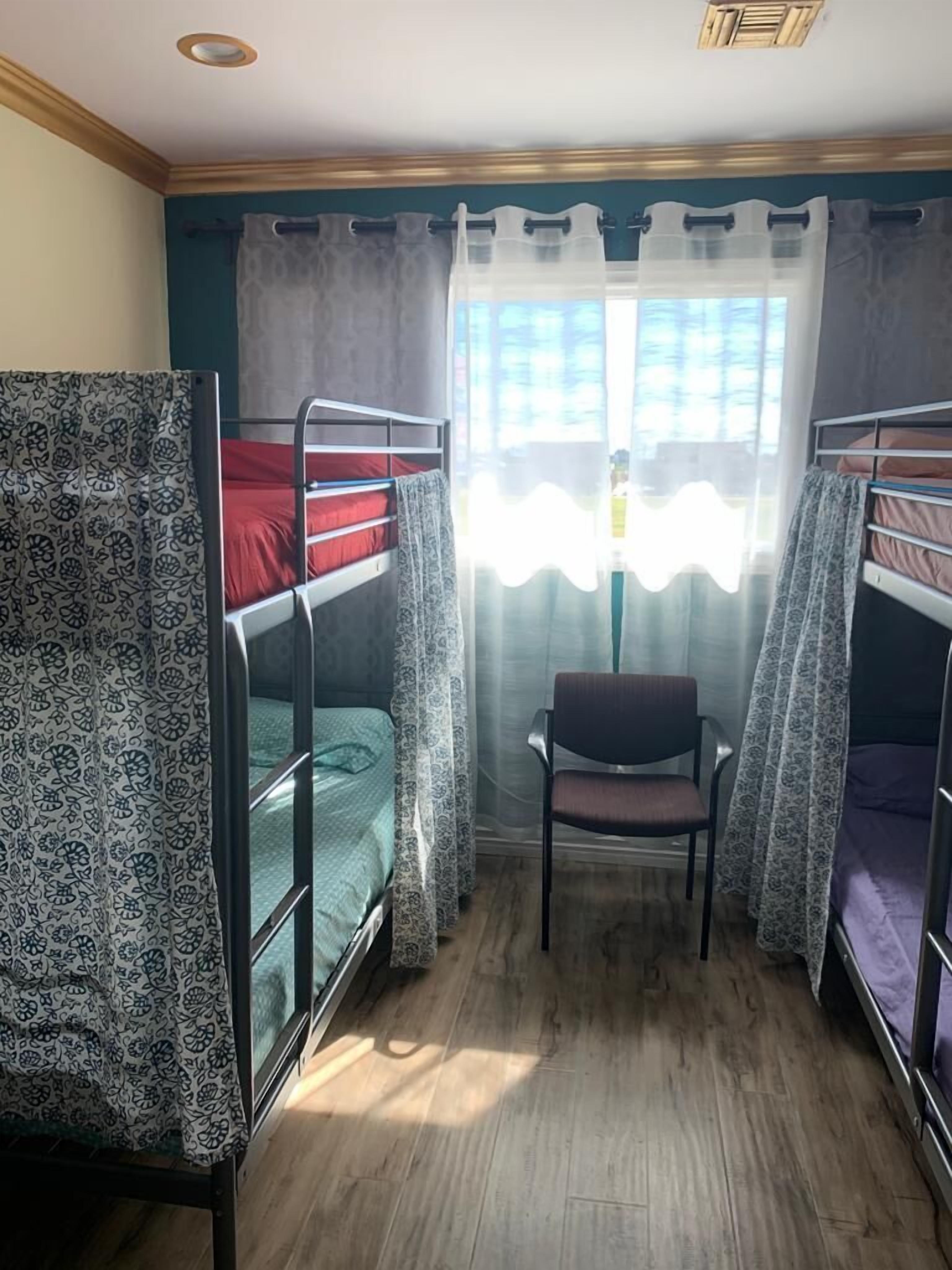 Une chambre de dortoir avec des lits superposés, une chaise et une fenêtre ornée de rideaux légers.