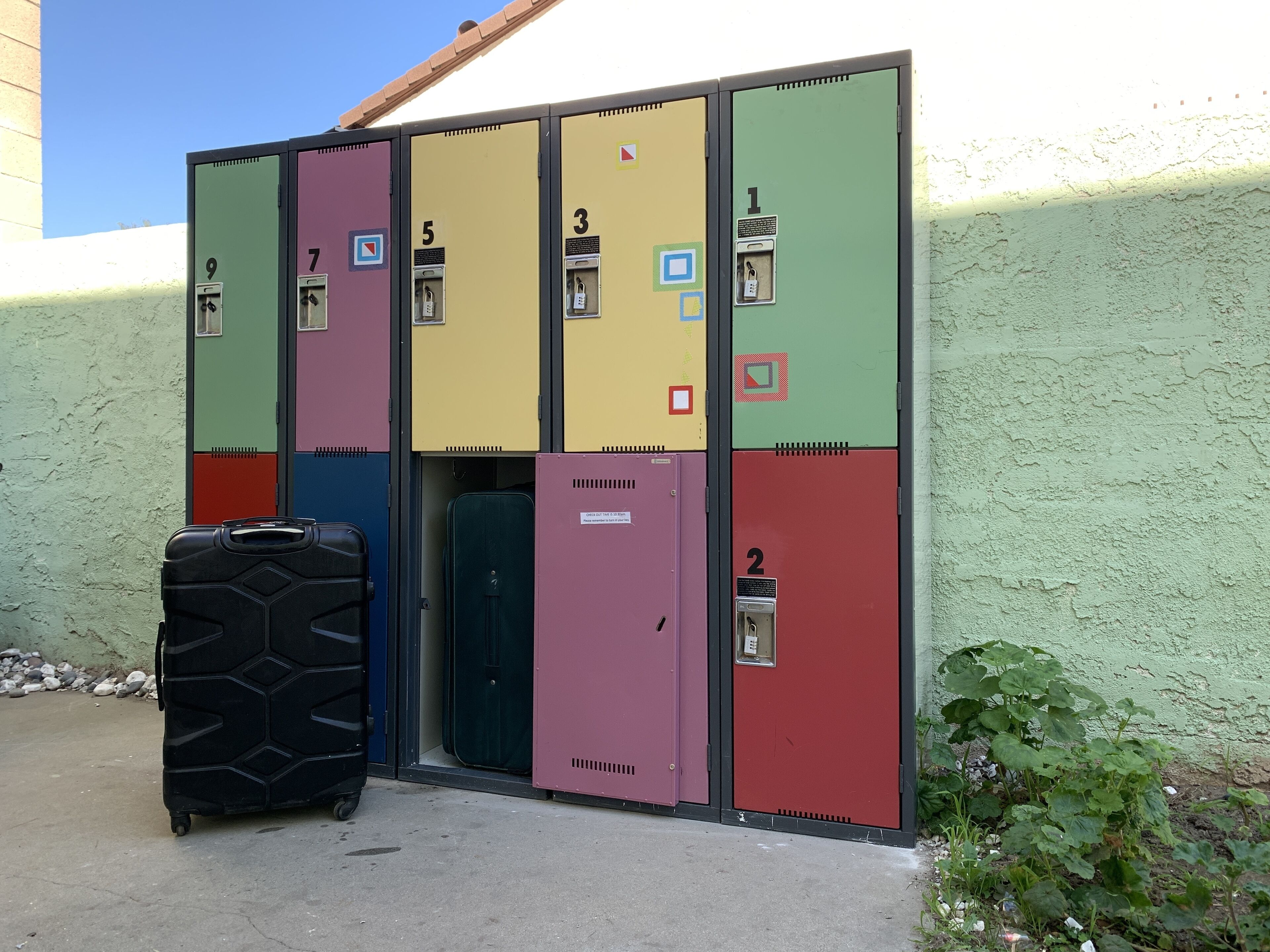 A row of colorful storage lockers with numbers 1 to 9, a black suitcase, and a green door.