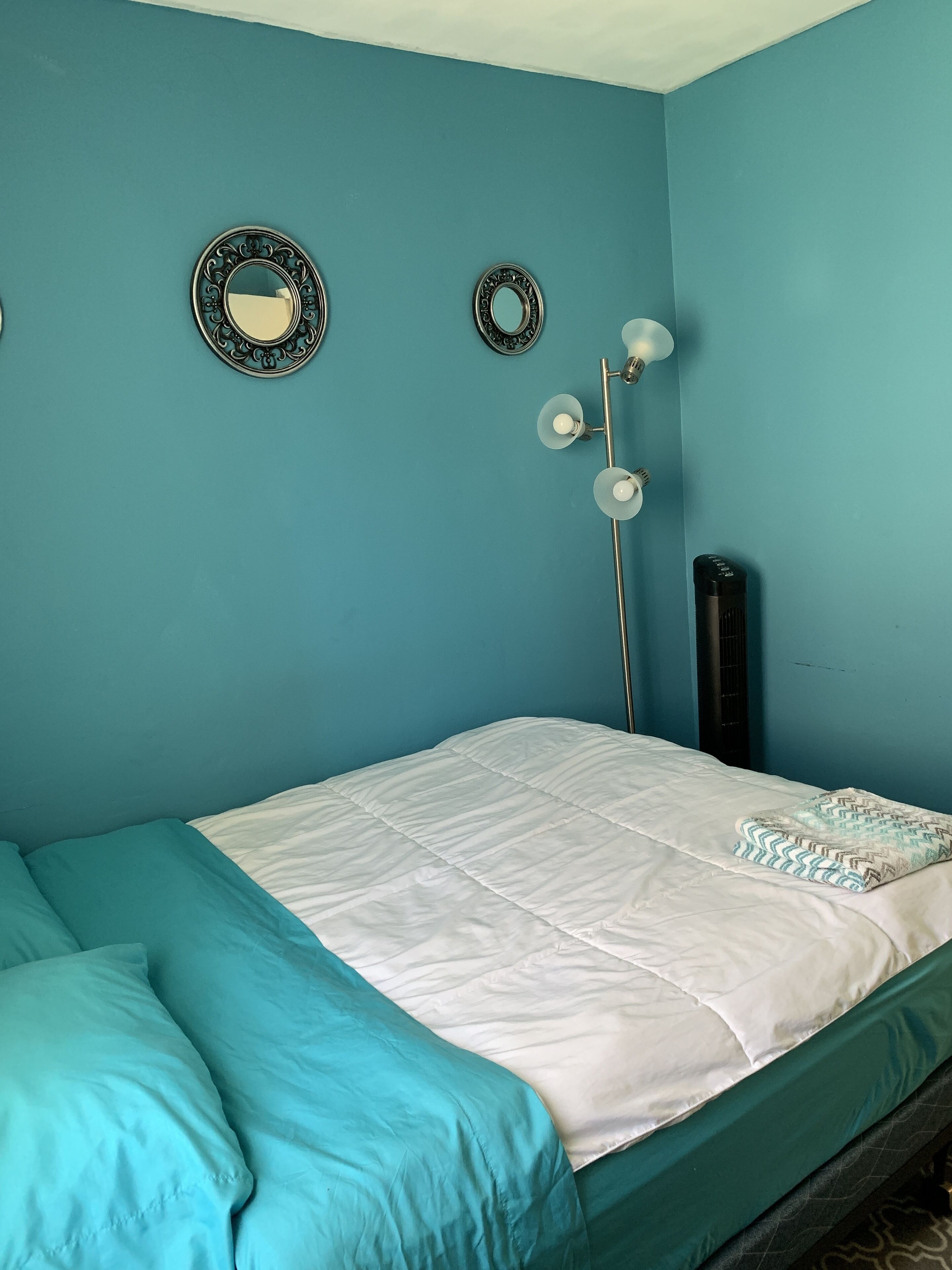 A room with teal walls, a bed with teal and white bedding, a black heater, and two wall-mounted mirrors.