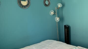 A room with teal walls, a bed with teal and white bedding, a black heater, and two wall-mounted mirrors.