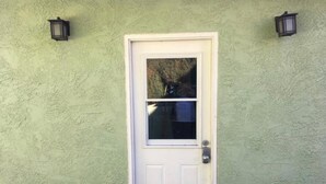 A white door with a glass panel, set in a textured green wall with two wall-mounted lanterns. - LAX guest house (Inglewood)