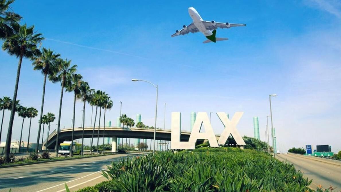 A road with a large 'LAX' sign, palm trees, and an airplane in the sky.