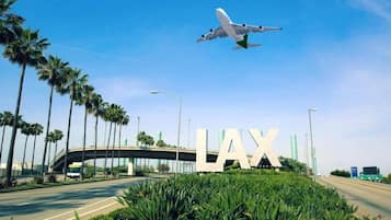 A road with a large 'LAX' sign, palm trees, and an airplane in the sky.