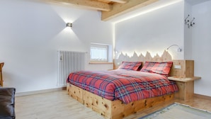 Et soveværelse med en træseng, en radiator, et vindue med gardiner og en vægmonteret lampe.