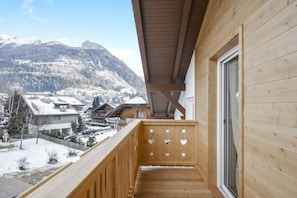 Un balcon en bois offrant une vue sur un village enneigé et sur les montagnes.
