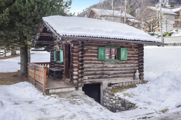 Une cabane en rondins dotée d’un porche et de fondations en pierre, entourée de neige.