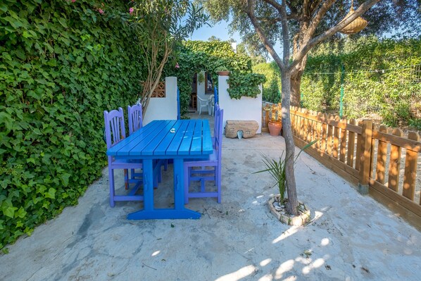 Eine Terrasse mit blauem Tisch und Stühlen, umgeben von einem Holzzaun und Grünpflanzen.