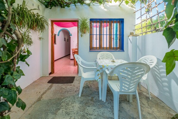 Un pequeño patio con una mesa y sillas, una ventana con rejas y plantas en macetas.
