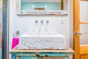 Ein Badezimmer mit einem weißen Waschbecken, zwei Wasserhähnen, einer Holztür und einem Spiegel über dem Waschbecken.