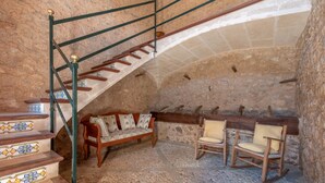 A stone-walled room with a wooden staircase, a cushioned bench, and two rocking chairs. - Secluded Villa with Pool, Wi-Fi, Air Conditioning and Terrace; Parking available (Alaró)