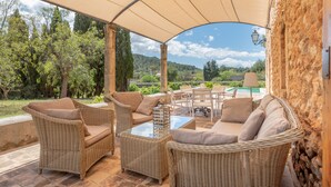 An outdoor patio with wicker furniture, a glass table, and a view of a pool and greenery. - Secluded Villa with Pool, Wi-Fi, Air Conditioning and Terrace; Parking available (Alaró)