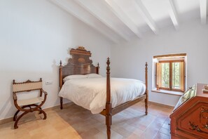 A bedroom with a wooden four-poster bed, a wooden chair, a window with a view, and a wooden dresser.