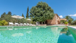A clear swimming pool with lounge chairs and umbrellas, surrounded by trees and a stone building. - Secluded Villa with Pool, Wi-Fi, Air Conditioning and Terrace; Parking available (Alaró)