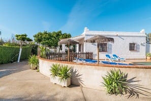 A white building with a pool, sun loungers, and potted plants.