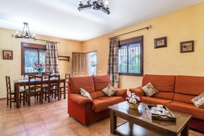 Una sala de estar con un sofá, una mesa de comedor con sillas, una mesa auxiliar y una araña.